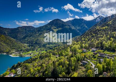 The Improbable aerial landscape of village Molveno, Italy, azure water of lake, empty beach, snow covered mountains Dolomites on background, roof top Stock Photo