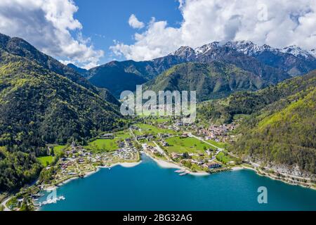 The Improbable aerial landscape of village Molveno, Italy, azure water of lake, empty beach, snow covered mountains Dolomites on background, roof top Stock Photo