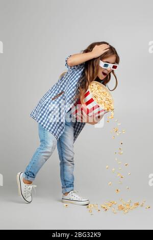 full length view of caucasian child girl in red-blue 3d glasses so hurried to the cinema that she dropped popcorn from a bucket onto the floor Stock Photo
