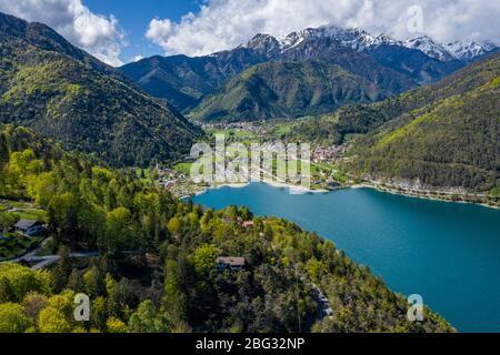 The Improbable aerial landscape of village Molveno, Italy, azure water of lake, empty beach, snow covered mountains Dolomites on background, roof top Stock Photo