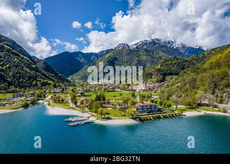 The Improbable aerial landscape of village Molveno, Italy, azure water of lake, empty beach, snow covered mountains Dolomites on background, roof top Stock Photo