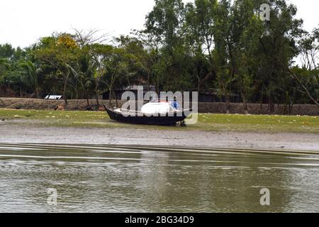 One small sized fishing boat ported on a small bank of a river side while the river is full of fresh water Stock Photo
