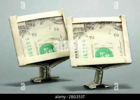 Dollars folded into computer monitors on grey background Stock Photo
