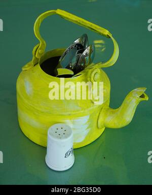 Kitchen utensils and cutlery in old fashioned green vintage teapot in bucket on table along with pepper shaker. Vintage Whistling kettle on green tabl Stock Photo