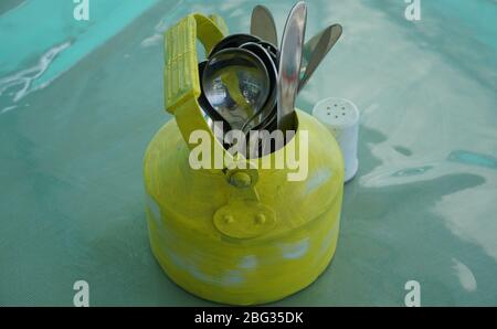 Kitchen utensils and cutlery in old fashioned green vintage teapot in bucket on table along with pepper shaker. Vintage Whistling kettle on green tabl Stock Photo