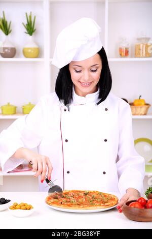 Beautiful girl chief-cooker with pizza on kitchen background Stock Photo