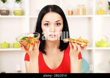 Pretty girl selects pizza or diet on kitchen background Stock Photo