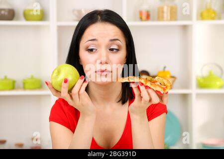 Pretty girl selects pizza or diet on kitchen background Stock Photo