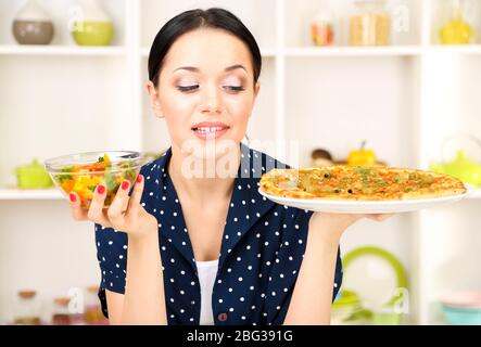 Pretty girl selects pizza or diet on kitchen background Stock Photo