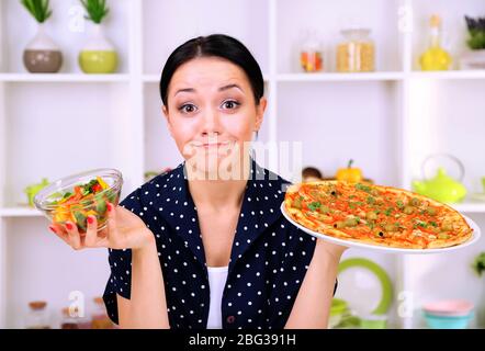 Pretty girl selects pizza or diet on kitchen background Stock Photo