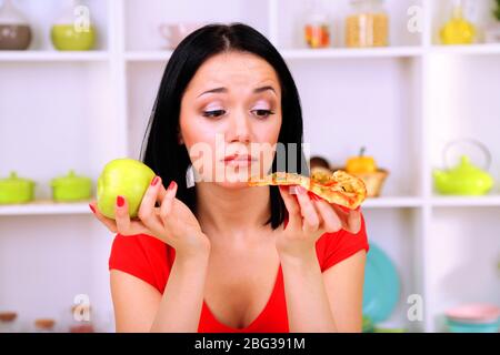 Pretty girl selects pizza or diet on kitchen background Stock Photo