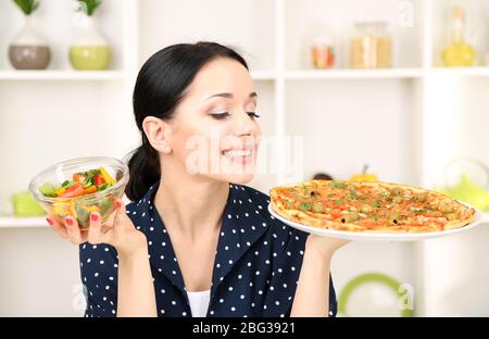 Pretty girl selects pizza or diet on kitchen background Stock Photo