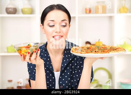 Pretty girl selects pizza or diet on kitchen background Stock Photo