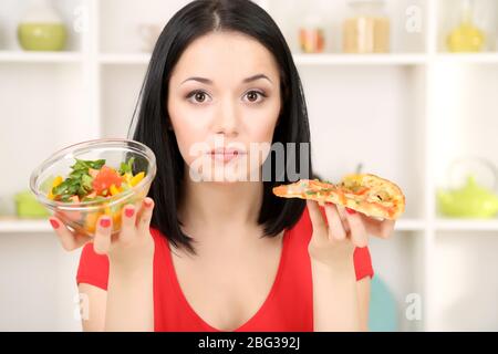 Pretty girl selects pizza or diet on kitchen background Stock Photo