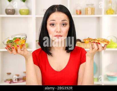 Pretty girl selects pizza or diet on kitchen background Stock Photo