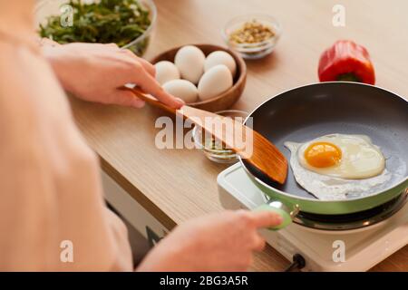 Warm-toned close up of unrecognizable young woman cooking eggs on frying pan while preparing healthy breakfast in morning, copy space Stock Photo