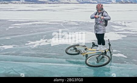 Woman stands near her bike on ice. The girl cyclist stopped to r Stock Photo