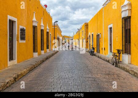 Cityscape with people on a Tricycle in the colorful yellow streets with colonial style architecture, Izamal, Mexico. Stock Photo