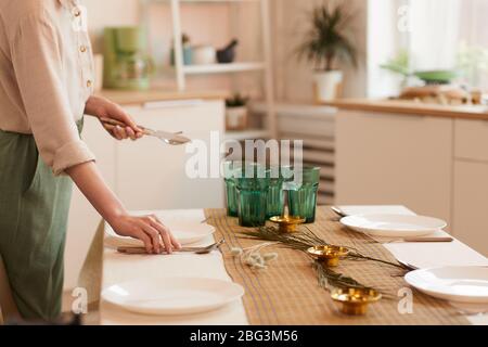 Warm toned side view portrait of young woman serving table in minimal kitchen interior, copy space Stock Photo