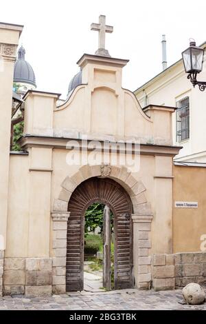 Ancient gates, entrance to church, cross on the top. Ancient building, an old door and arch. Architectural heritage in Lviv, Ukraine. Stock Photo