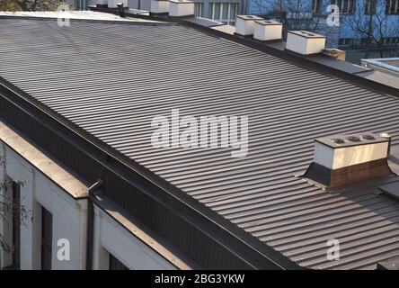 The roof is covered with metal, painted panels. Large building roof area. Stock Photo