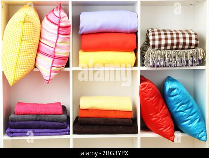 Bright pillows, towels and plaids on shelves, isolated on white Stock Photo