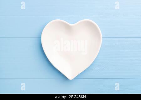 Heart shaped empty white plate on blue wooden plank background. Table setting for Valentine's Day holiday. Close-up. Love concept Stock Photo