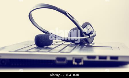 Retro image of black headset on laptop keyboard. Conceptual of customer support or online chat, discussion or conference. Stock Photo