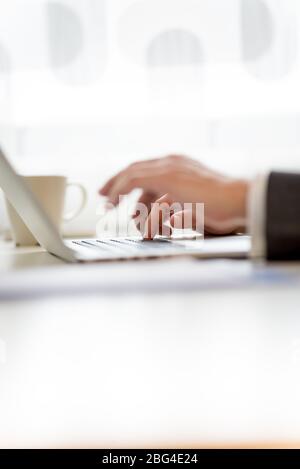Man typing in information on his laptop with selective focus to the hand furthest from the camera, side view of both hands on the desk. Stock Photo