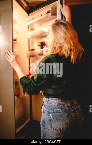 Young hungry woman looking in open fridge at night at home Stock Photo
