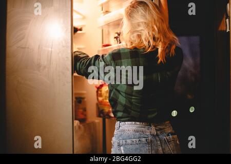 Young hungry woman looking for food in fridge at night at home Stock Photo