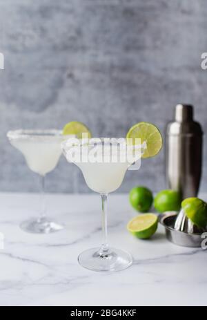 Two margarita cocktails with limes and shaker on white marble counter Stock Photo