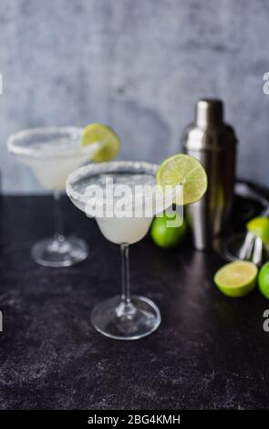 Two margarita cocktails with limes and shaker on black counter Stock Photo