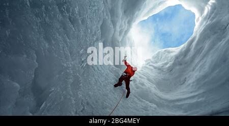 man climbing towards an opening in an icecave at Langjokull glacier Stock Photo