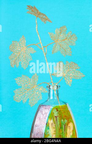 artificial golden plastic twig of tree in handpainted glass brandy bottle on aquamarine pastel color background Stock Photo