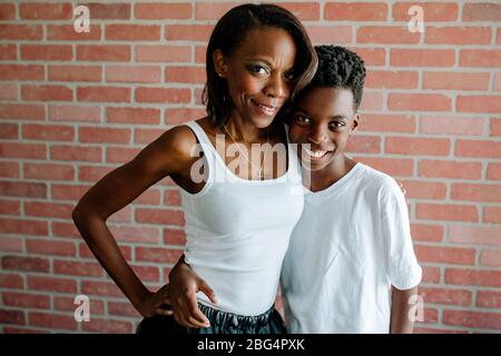 Pretty black mom hugging smiling preteen son in front of brick wall Stock Photo