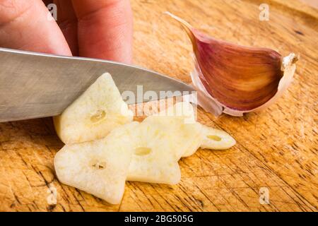 hand slicing garlic cloves on the cutting board with a knife Stock Photo