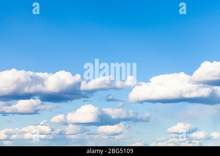 many low small cumulus clouds in blue sky on March day Stock Photo