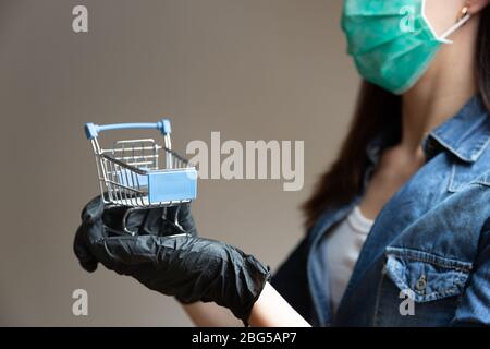 Woman wearing facial medical holding in hands with black gloves shopping cart. Shopping in pandemic concept Stock Photo