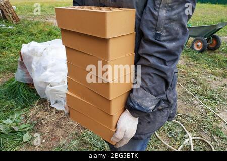 Piles of orange bricks, stacked in rows, the worker carries several pieces.2020 Stock Photo