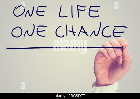 Retro instagram style image of a male hand writing phrase One life one chance on virtual screen. Stock Photo