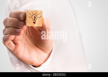 Man holding a small wooden cube with a hand-drawn illuminated light bulb conceptual of inspiration, imagination and innovation, with copyspace. Stock Photo