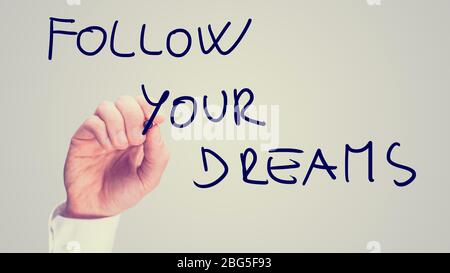 Retro instagram style image of a male hand writing motivational message Follow your dreams on virtual board. Stock Photo