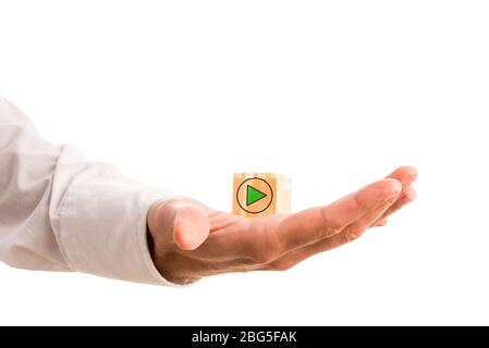 Green arrow icon in a circle pointing to the right of the frame on a wooden cube in a mans hand in a conceptual image, isolated on white with copyspac Stock Photo