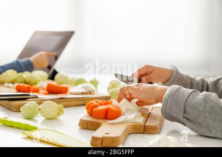 A girl's hands preparing food in the kitchen while her brother looks at the tablet Stock Photo