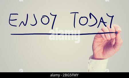 Retro instagram style image of a male hand writing Enjoy today on virtual screen. Stock Photo