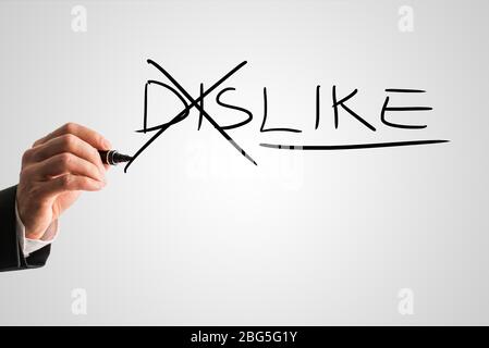 Man crossing through the Dis in the handwritten word Dislike on a virtual screen with a marker pen in a concept of opposites for Dislike - Like. Stock Photo