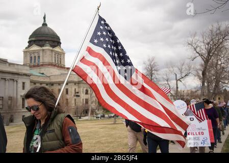 Helena, Montana - April 19, 2020: A woman at a protest holding an American flag walking with a large group of people protesting the government shutdow Stock Photo