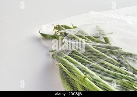 Green beans in sustainable grocery mesh bag. Vegetables in reusable eco friendly packaging on light background. Zero waste shopping, plastic free. Stock Photo