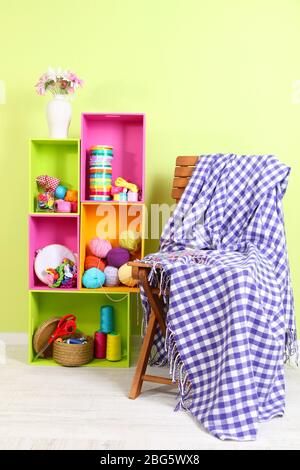 Colorful shelves of different colors with utensils near chair with plaid on wall background Stock Photo